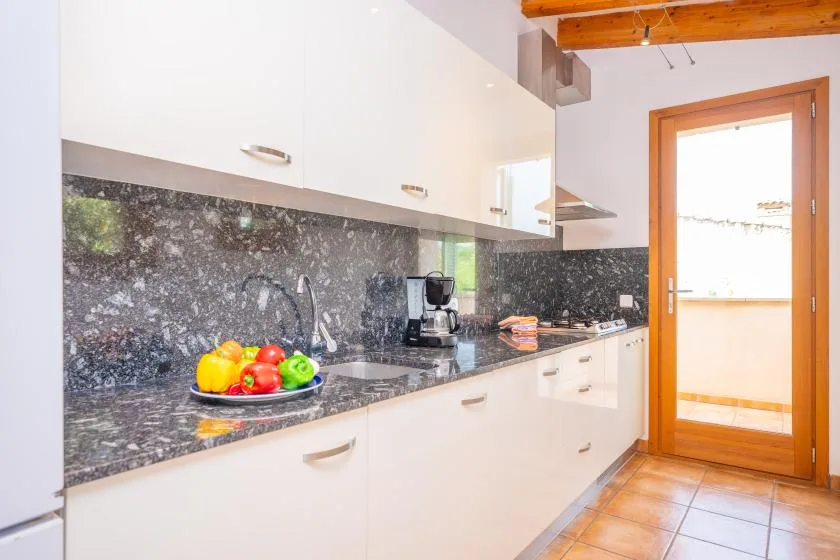 A bright kitchen with white cabinets, dark countertops, and a bowl of fruit.