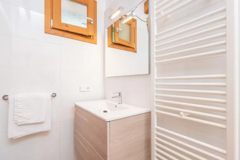 A bright bathroom with a sink, mirror, and white towel warmer.