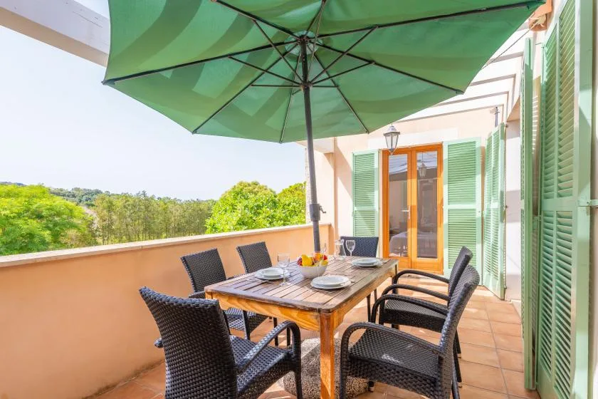An outdoor dining area with a wooden table and chairs beneath a green umbrella.