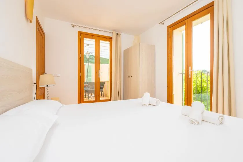 A bright bedroom with a bed beside tall windows opening onto a balcony.