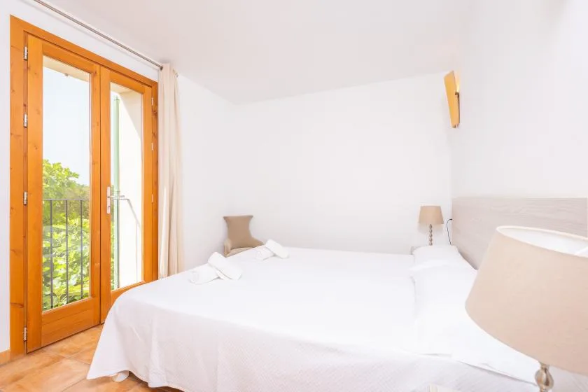 A bright bedroom with a white bed beside tall glass doors.