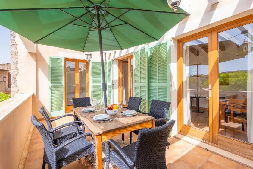 A sunny outdoor dining patio with a table and chairs beneath a green umbrella.