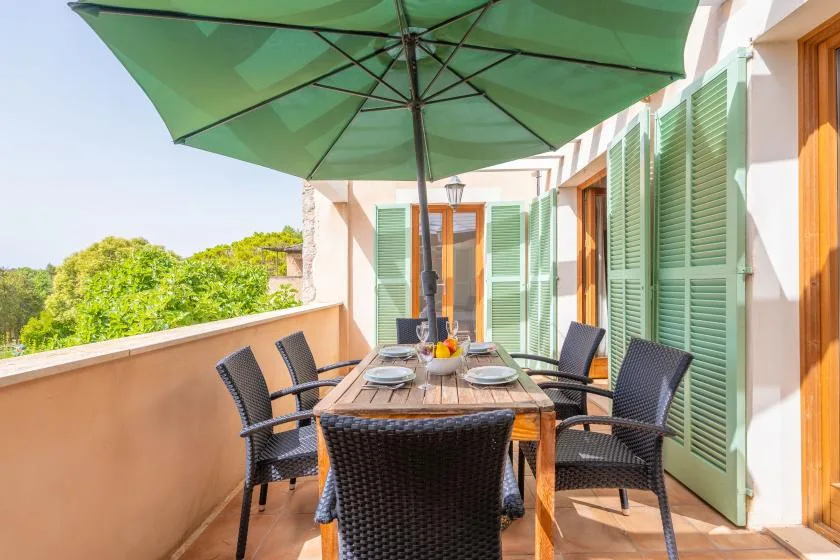 A sunny terrace dining area with a table beneath a large green umbrella.
