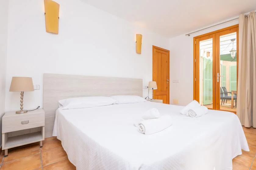 A bright bedroom with a neatly made bed and wooden-framed glass doors.