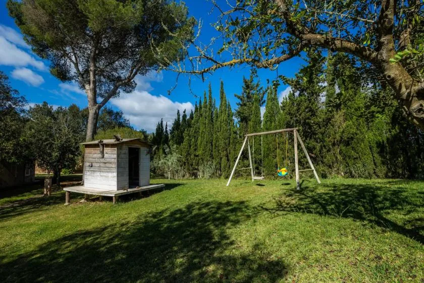 A grassy outdoor play area has a small wooden playhouse and a swing set.