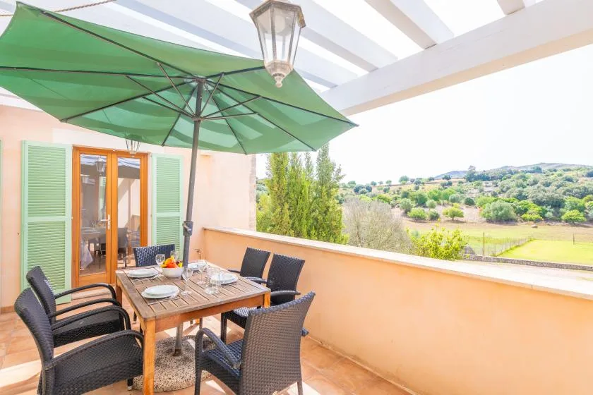 A covered outdoor dining area with a table and green umbrella overlooks a hillside landscape.