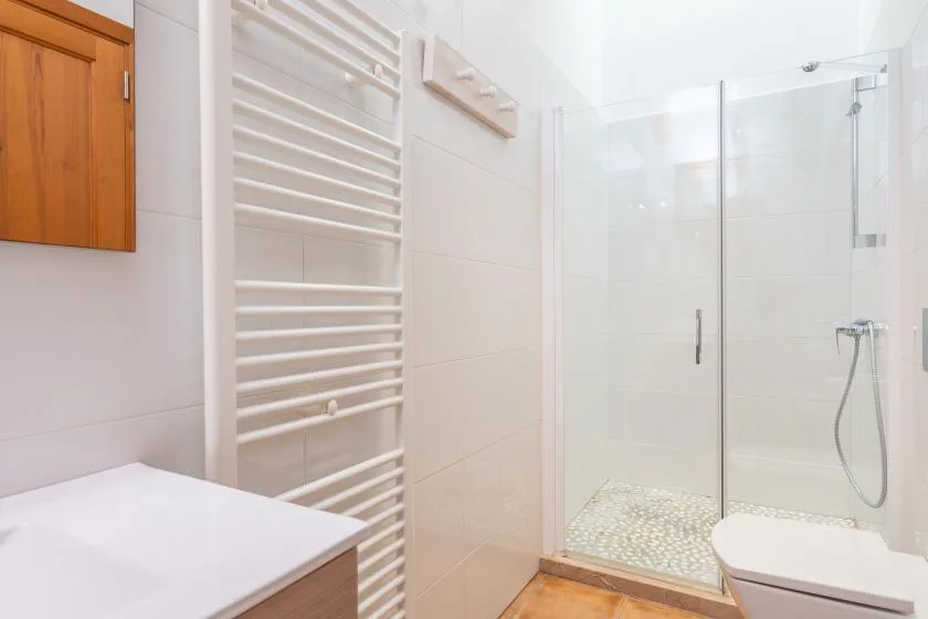 A bright bathroom with a glass shower and white tiled walls.