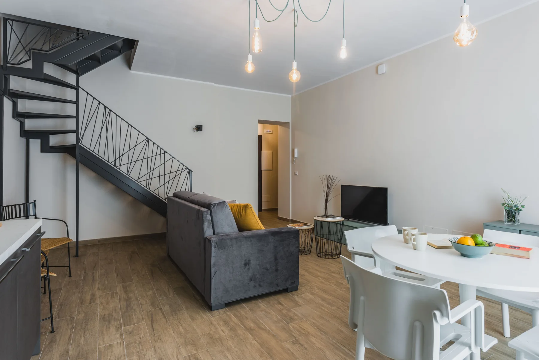Sala de estar y comedor con una escalera, asientos y un televisor.
