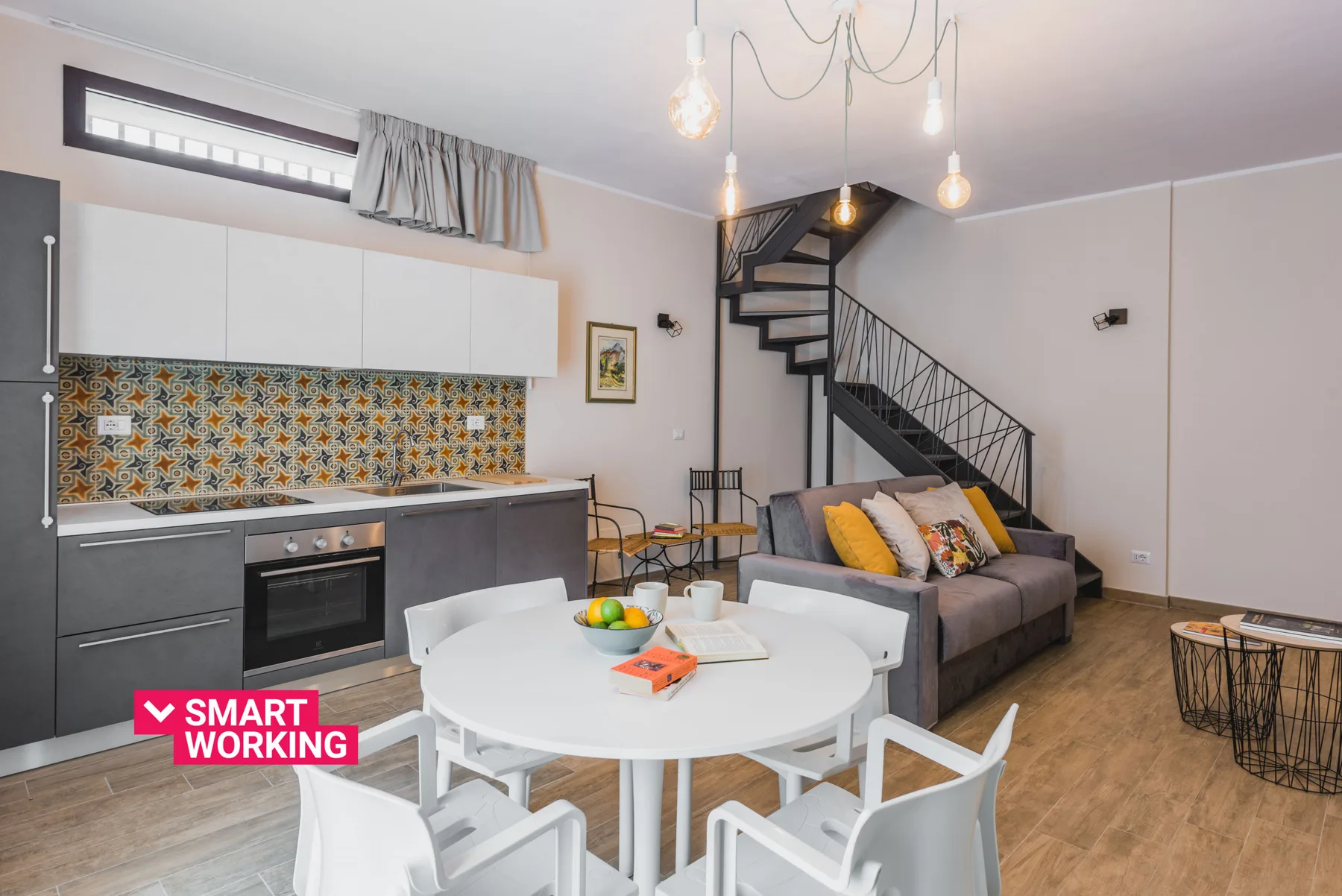 Una zona de comedor y estar con una mesa blanca, asientos y una escalera.