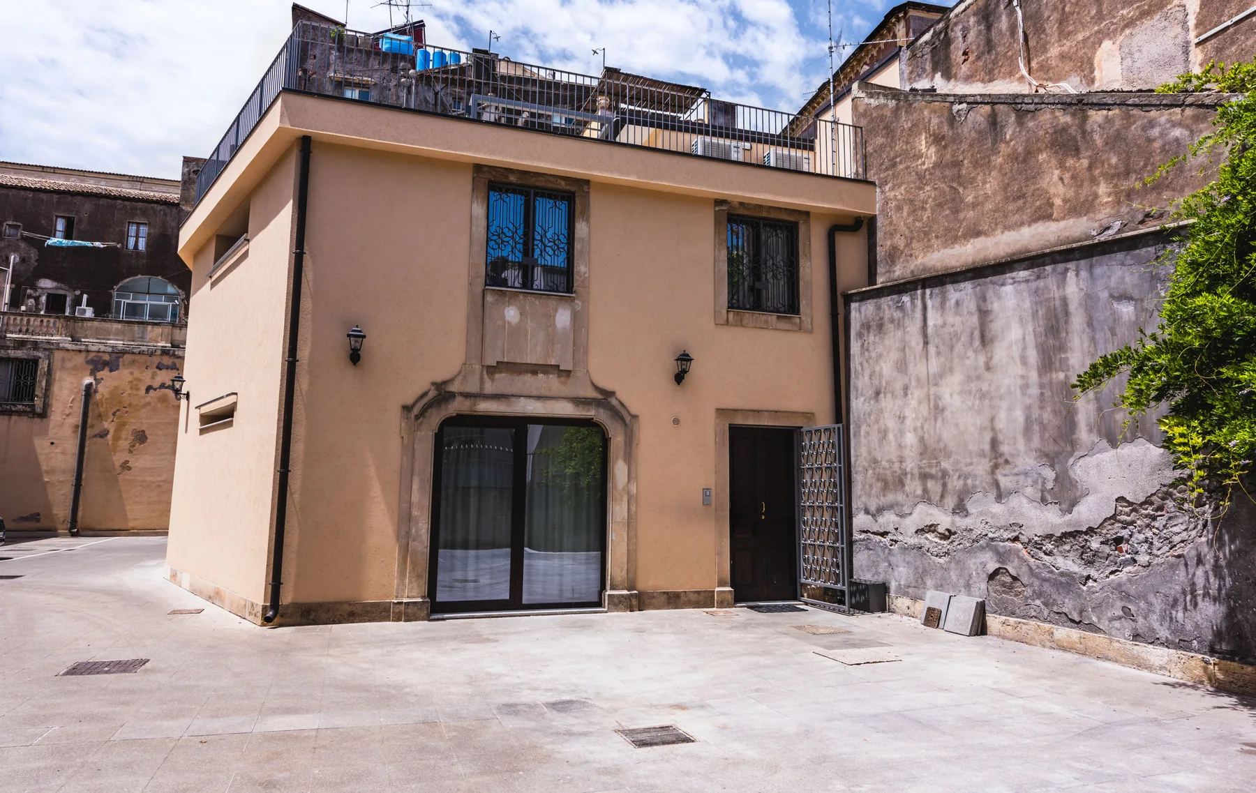 Un edificio beige de dos plantas da a un patio pavimentado, con una terraza en la azotea.