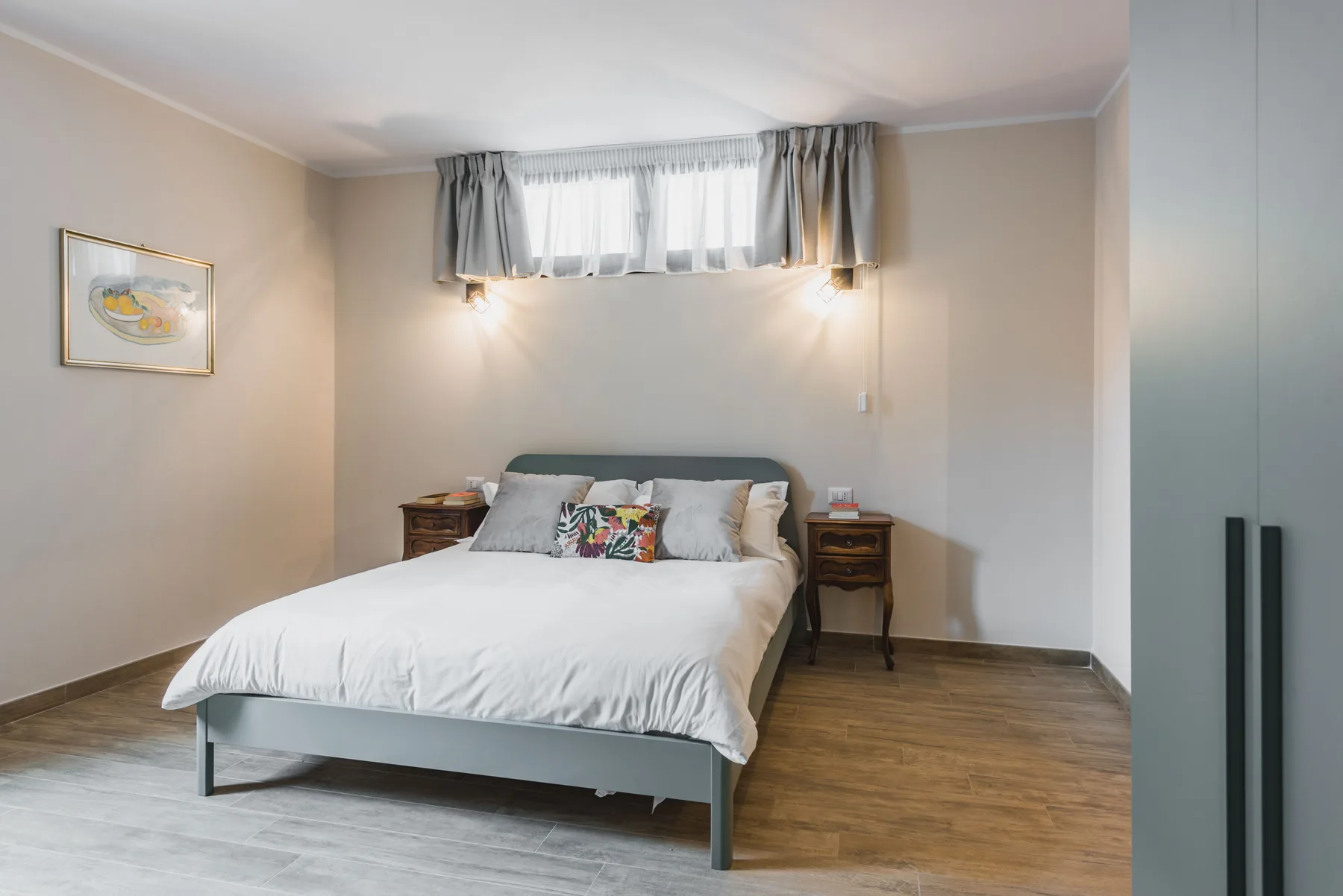 Un dormitorio con una cama bien tendida bajo una amplia ventana con cortinas.