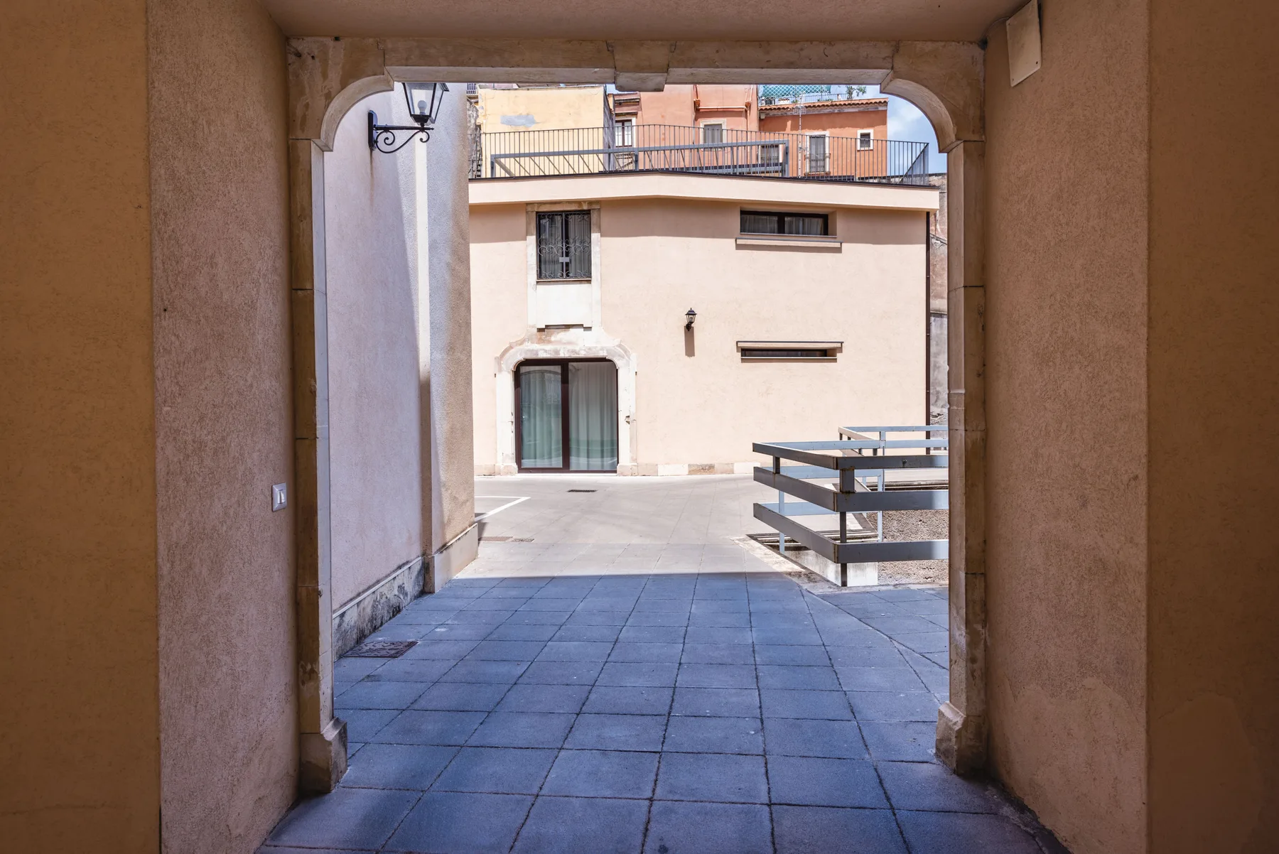 Un pasaje cubierto da a un patio pavimentado junto a un edificio de color claro.