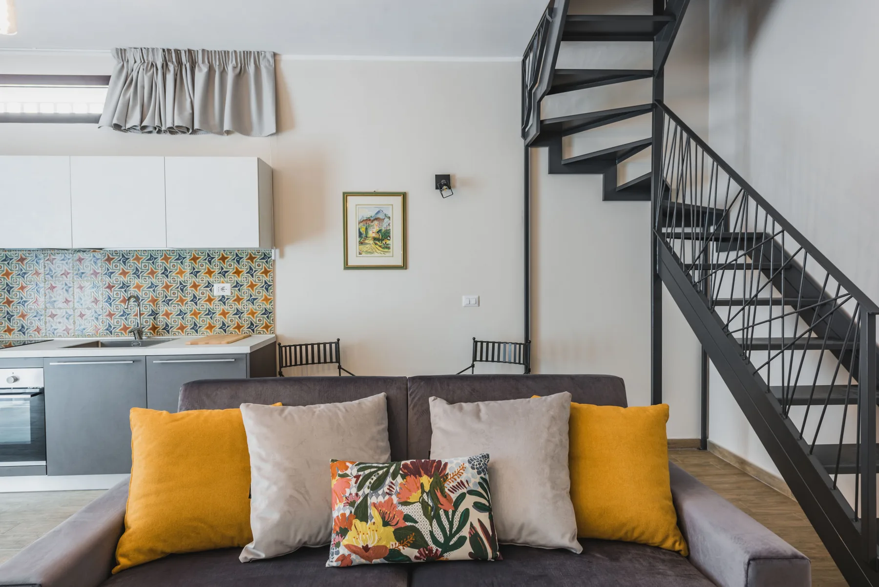 Una sala de estar con un sofá frente a una cocina compacta y una escalera.
