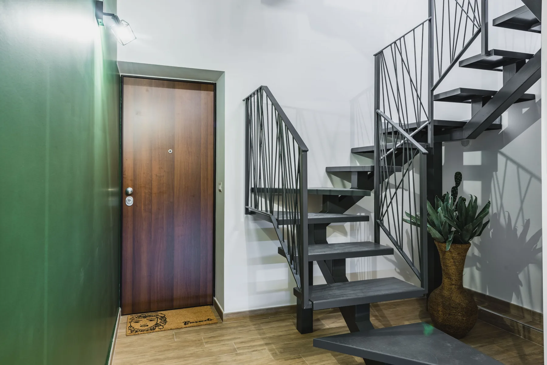 Una escalera interior con barandillas metálicas oscuras está junto a una puerta de madera.