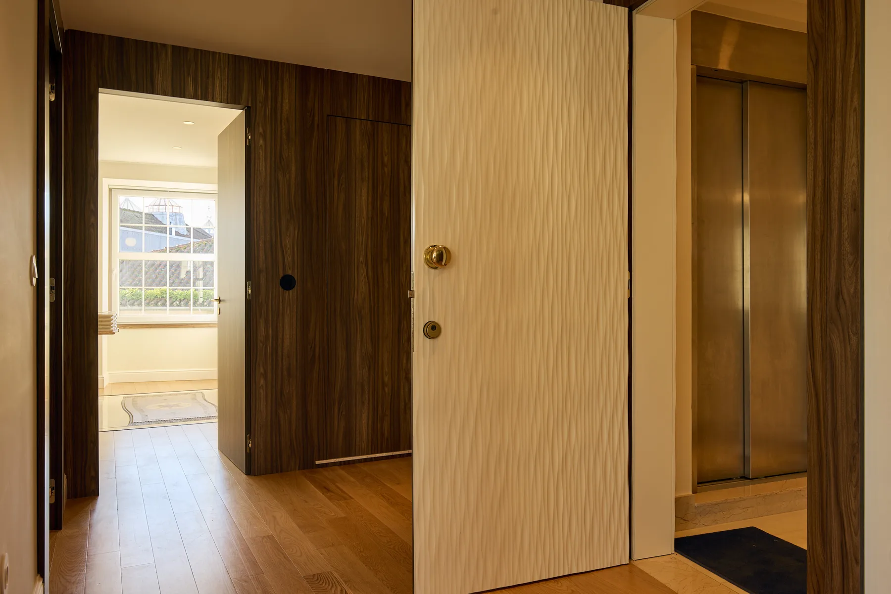 A wood-floored interior hallway opens toward a bright room with a large window.