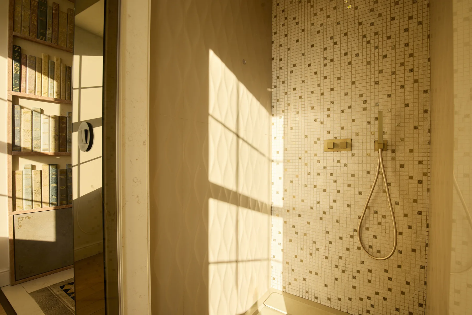 A tiled shower area beside a glass partition, lit by sunlight.