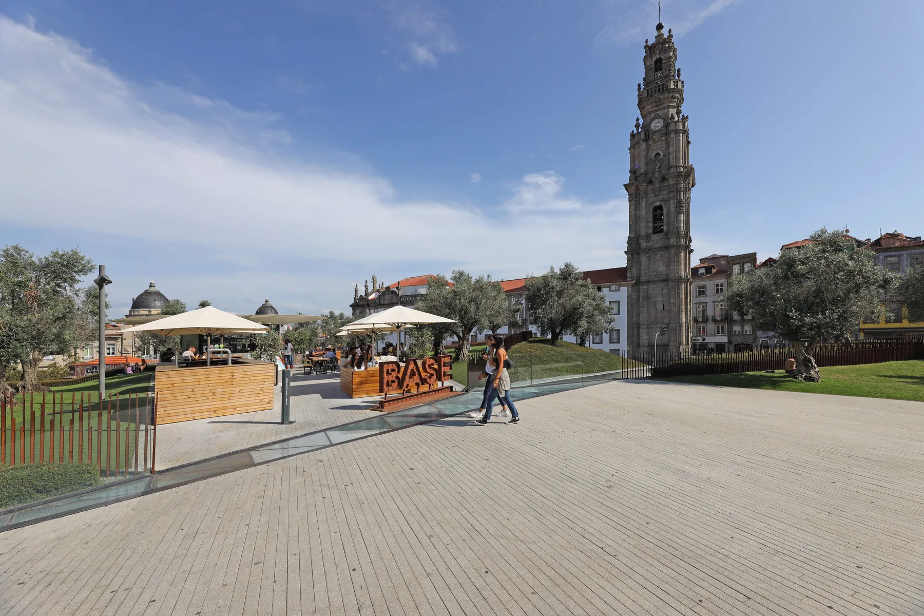 A paved public square with a tall stone tower and outdoor café seating.