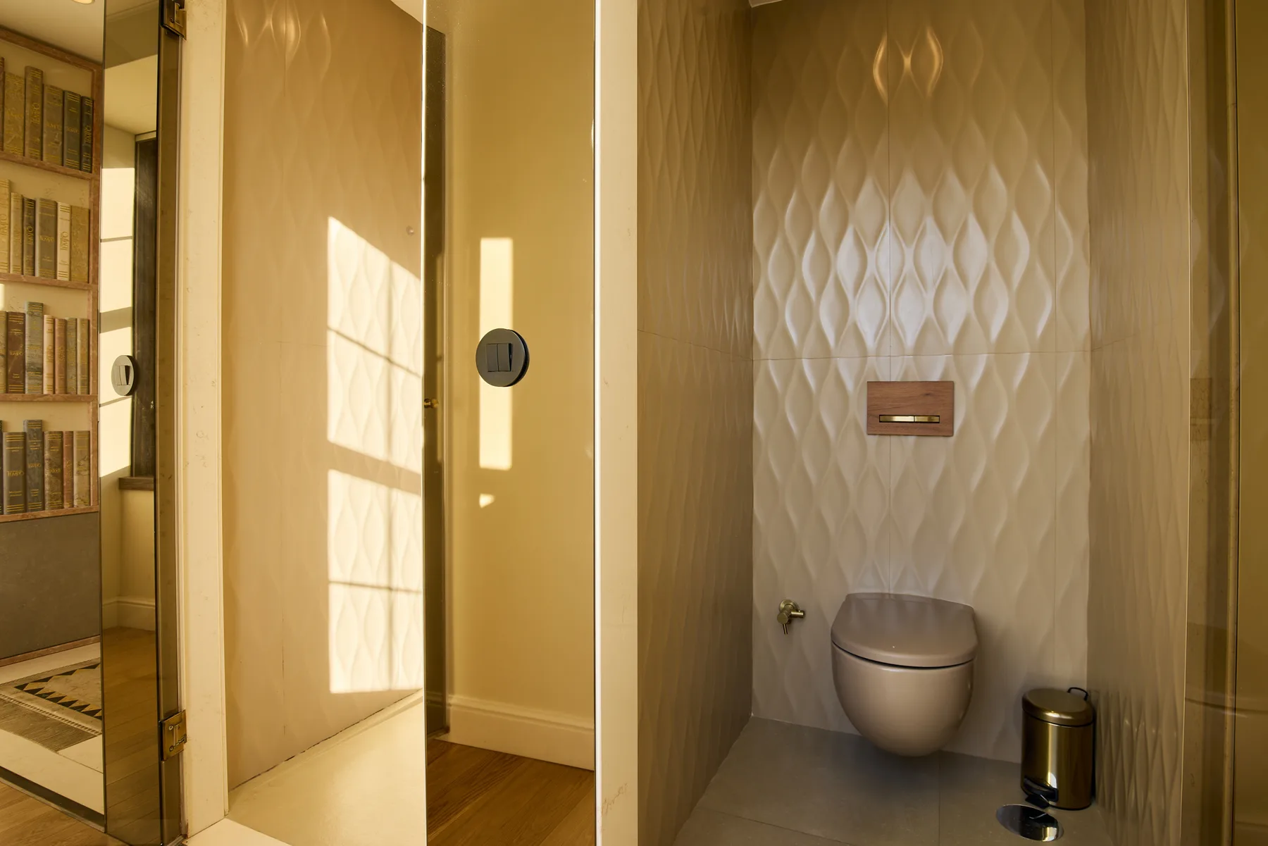 A bathroom with a wall-mounted toilet and patterned wall tiles.