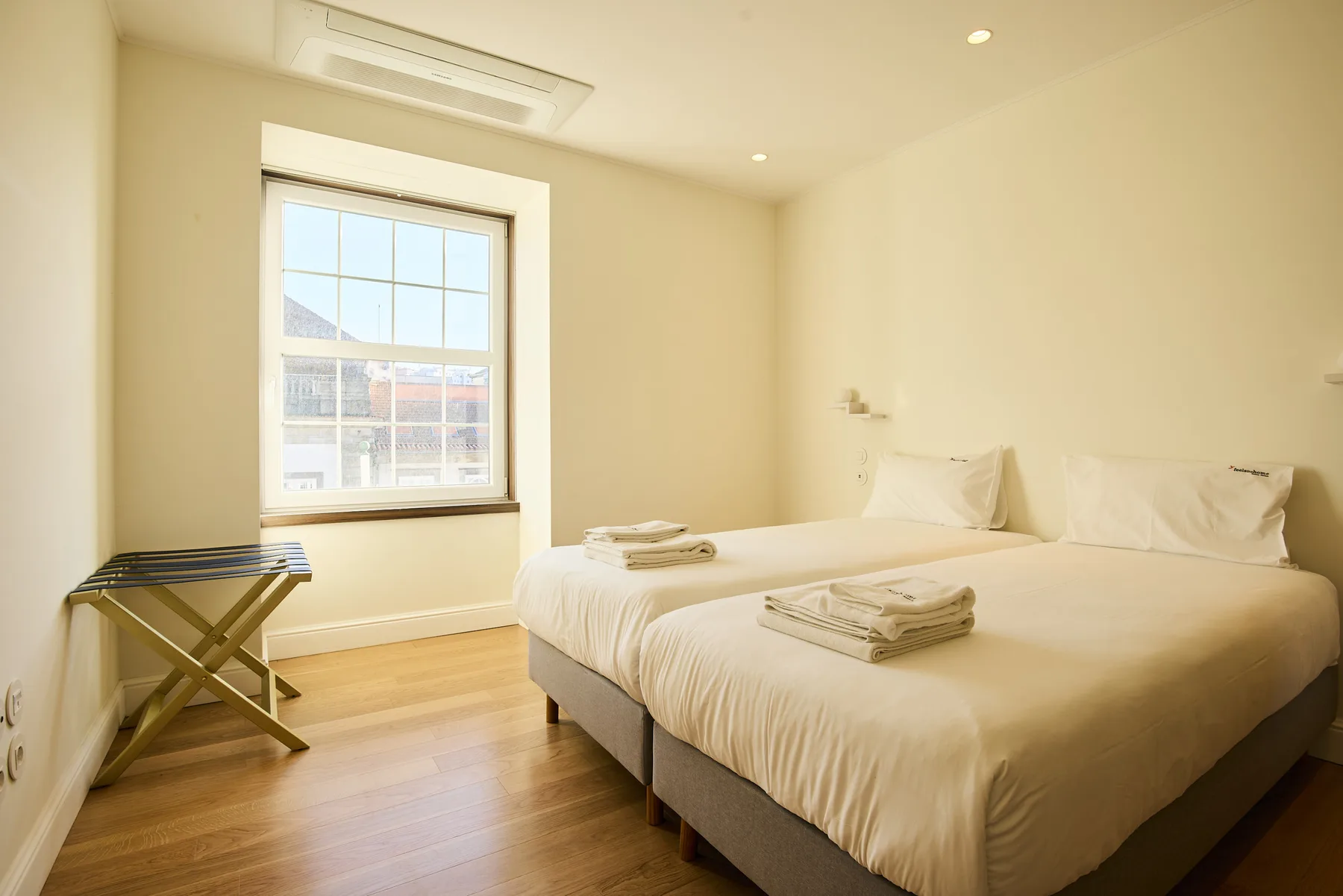 A bright bedroom with a large bed and a window overlooking nearby buildings.