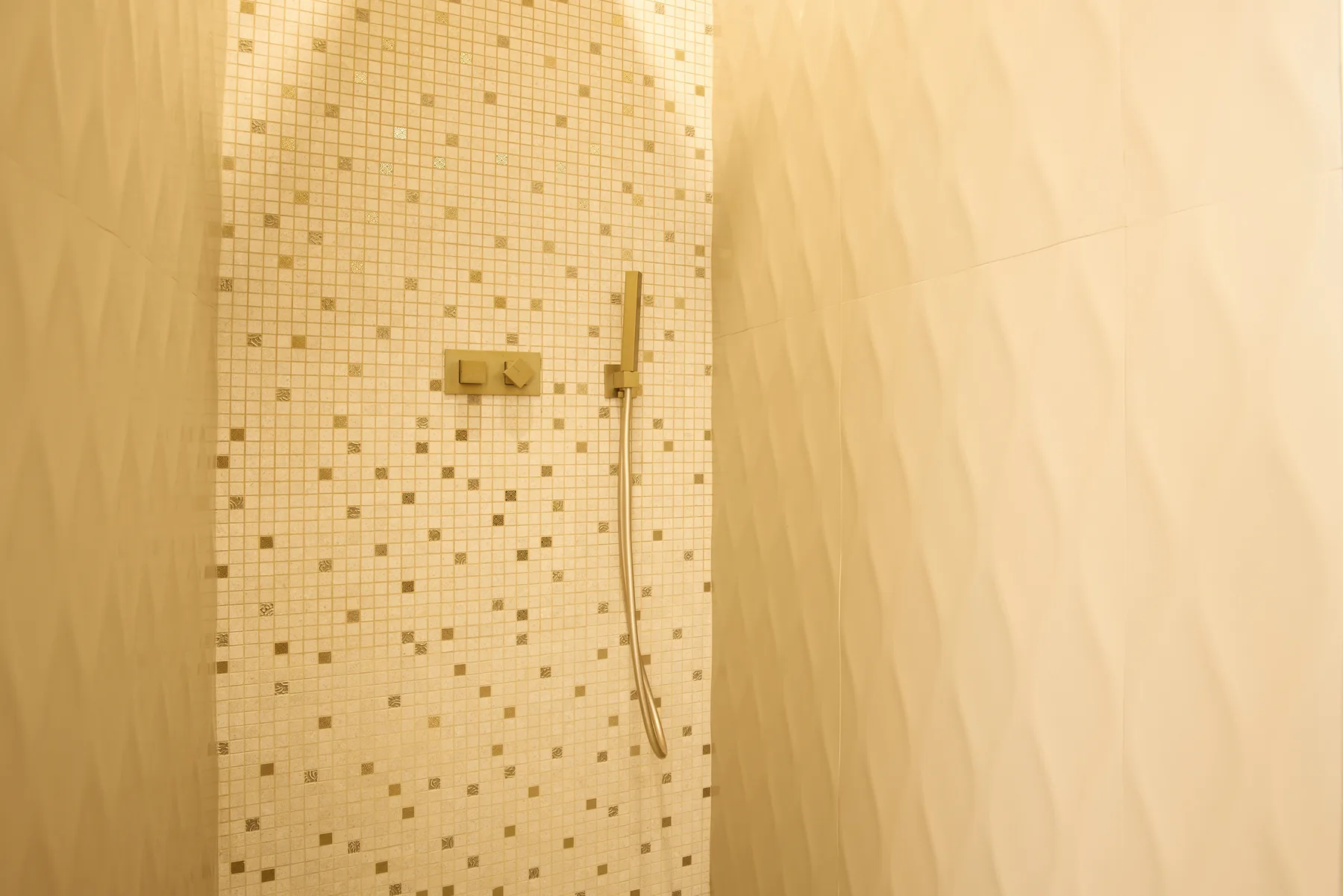 A shower with a handheld showerhead and a tiled wall.