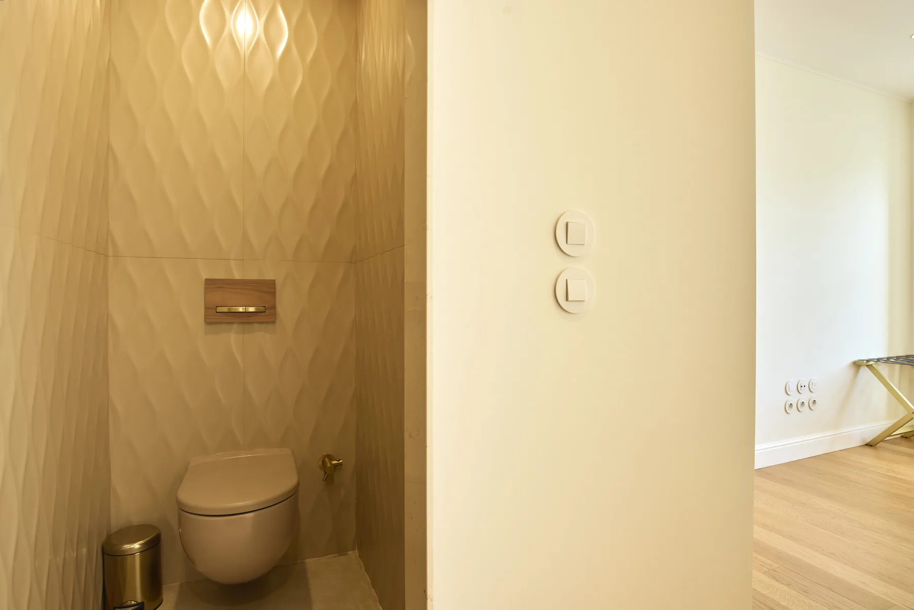A bathroom with a toilet and a textured wall beside a bright hallway.