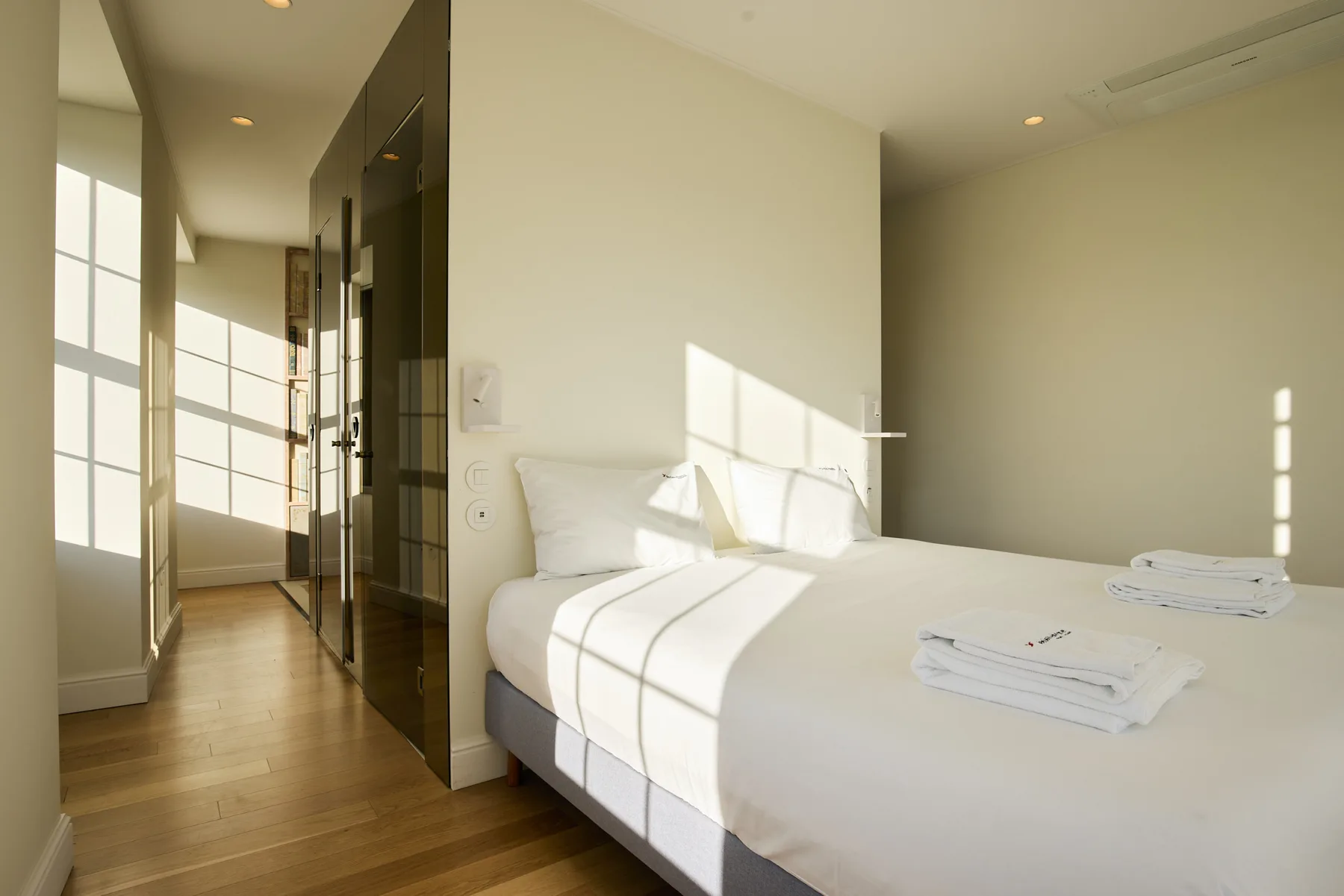 A bright bedroom with a neatly made bed and folded towels.