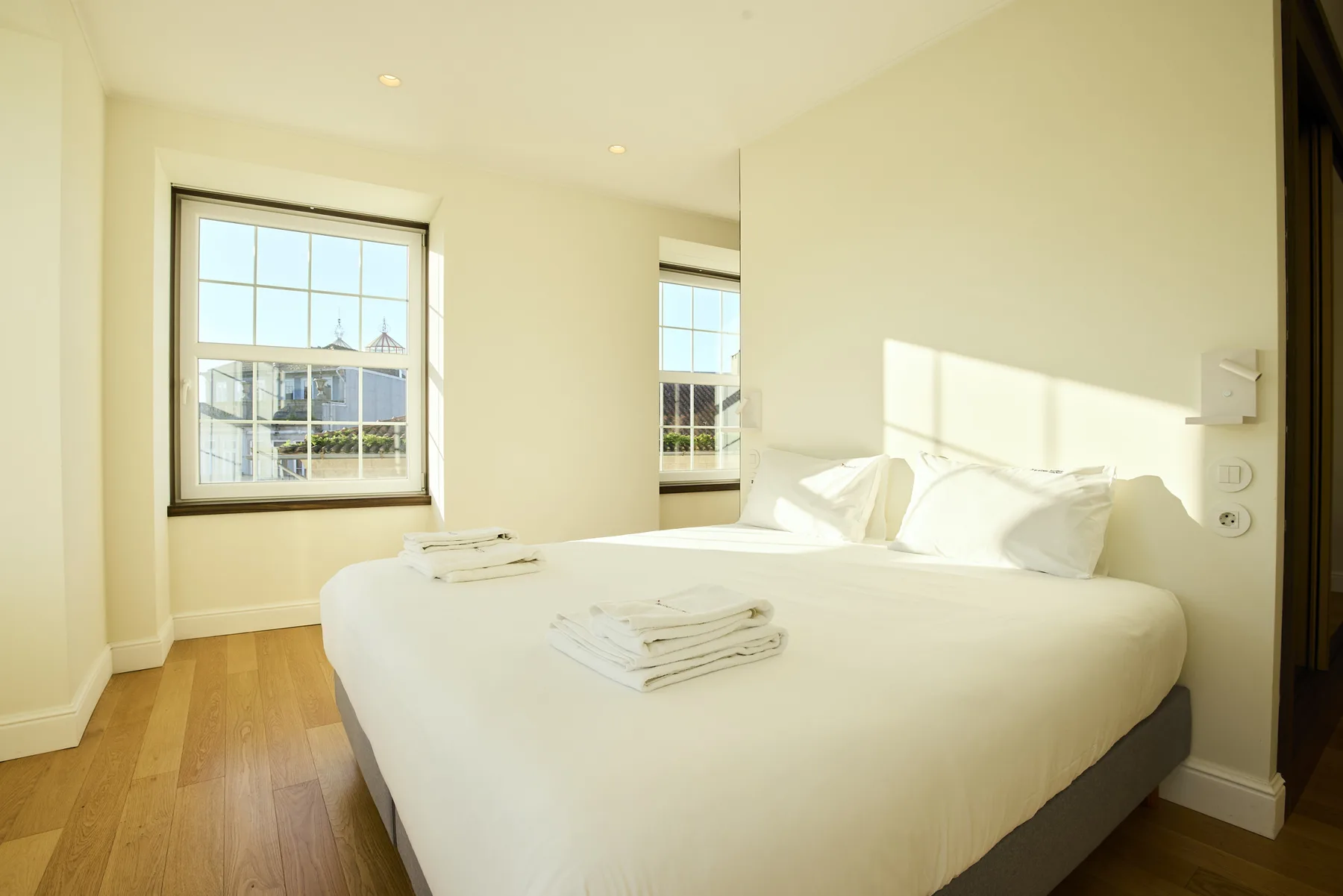 A bright bedroom with white bedding and sunlight coming through the windows.