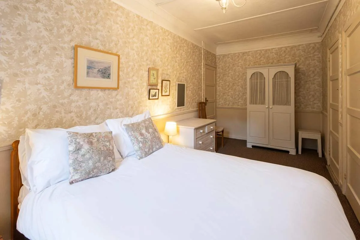 A bedroom with a neatly made bed, bedside table, and wardrobe.