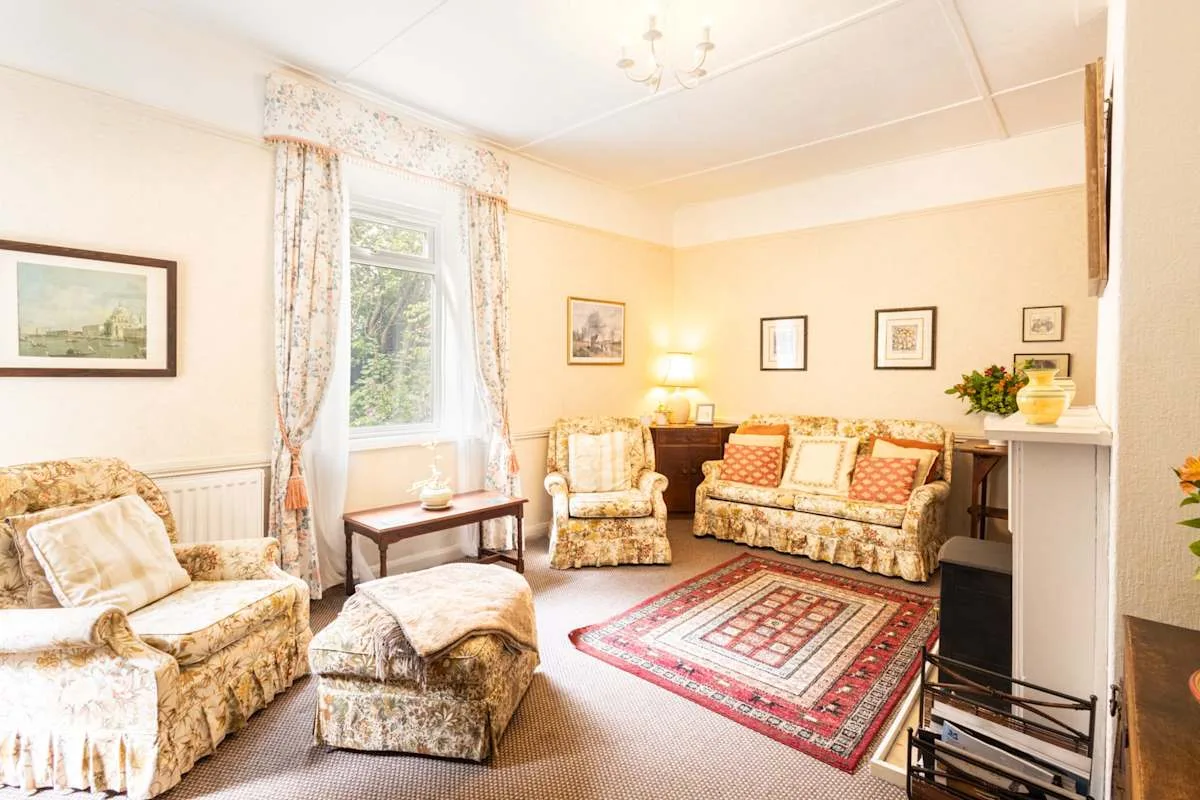 A bright sitting room with patterned seating around a red rug.