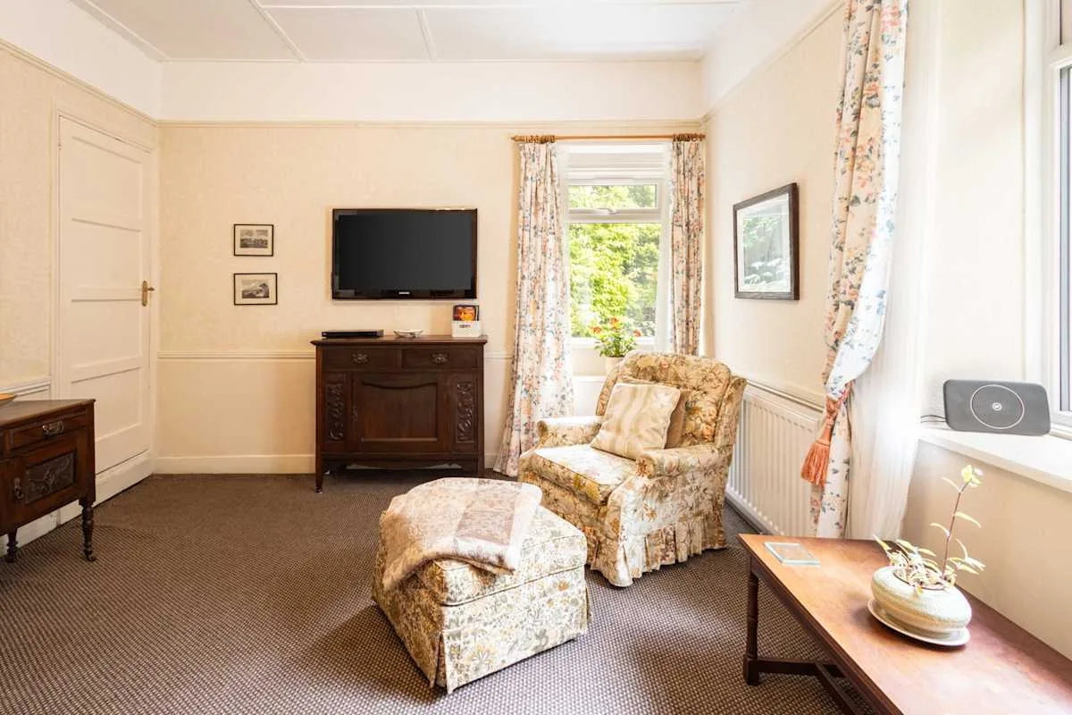 A sitting room with patterned seating, a television, and a window overlooking greenery.