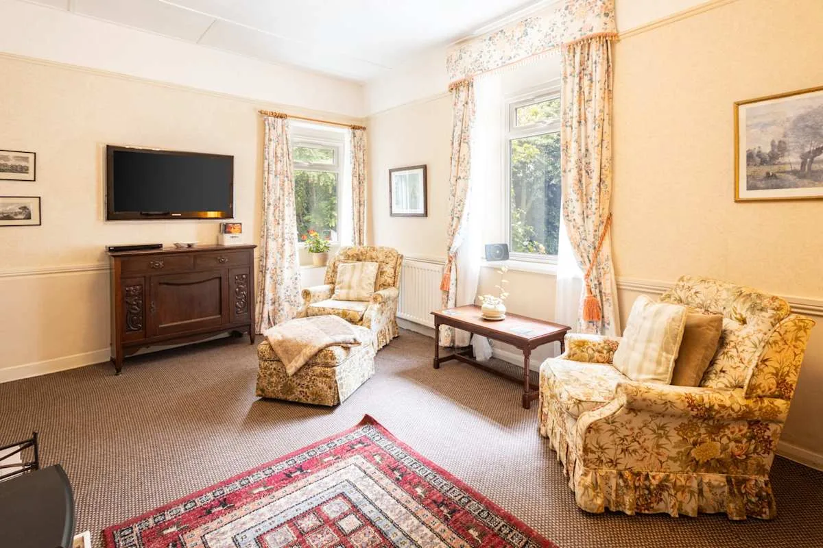 A sitting room with floral seating, a television, and a patterned rug.