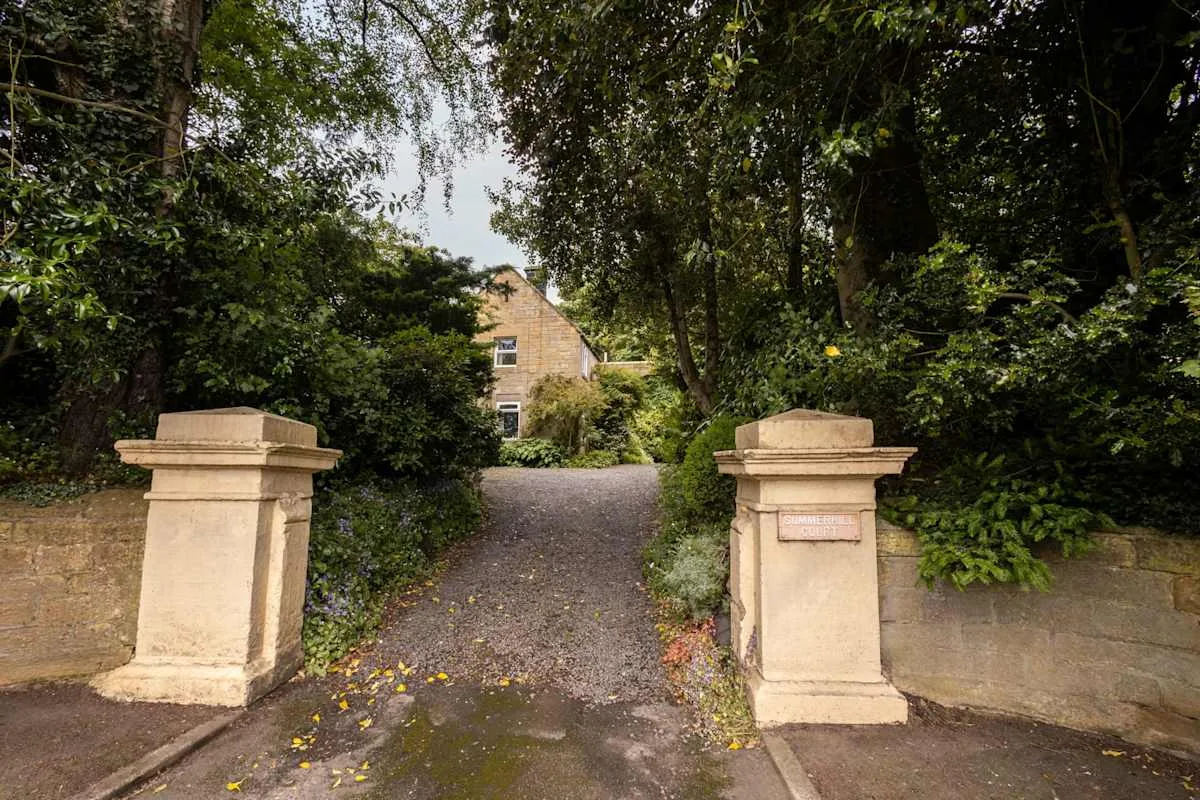 A gravel driveway runs between stone entrance pillars toward a house.