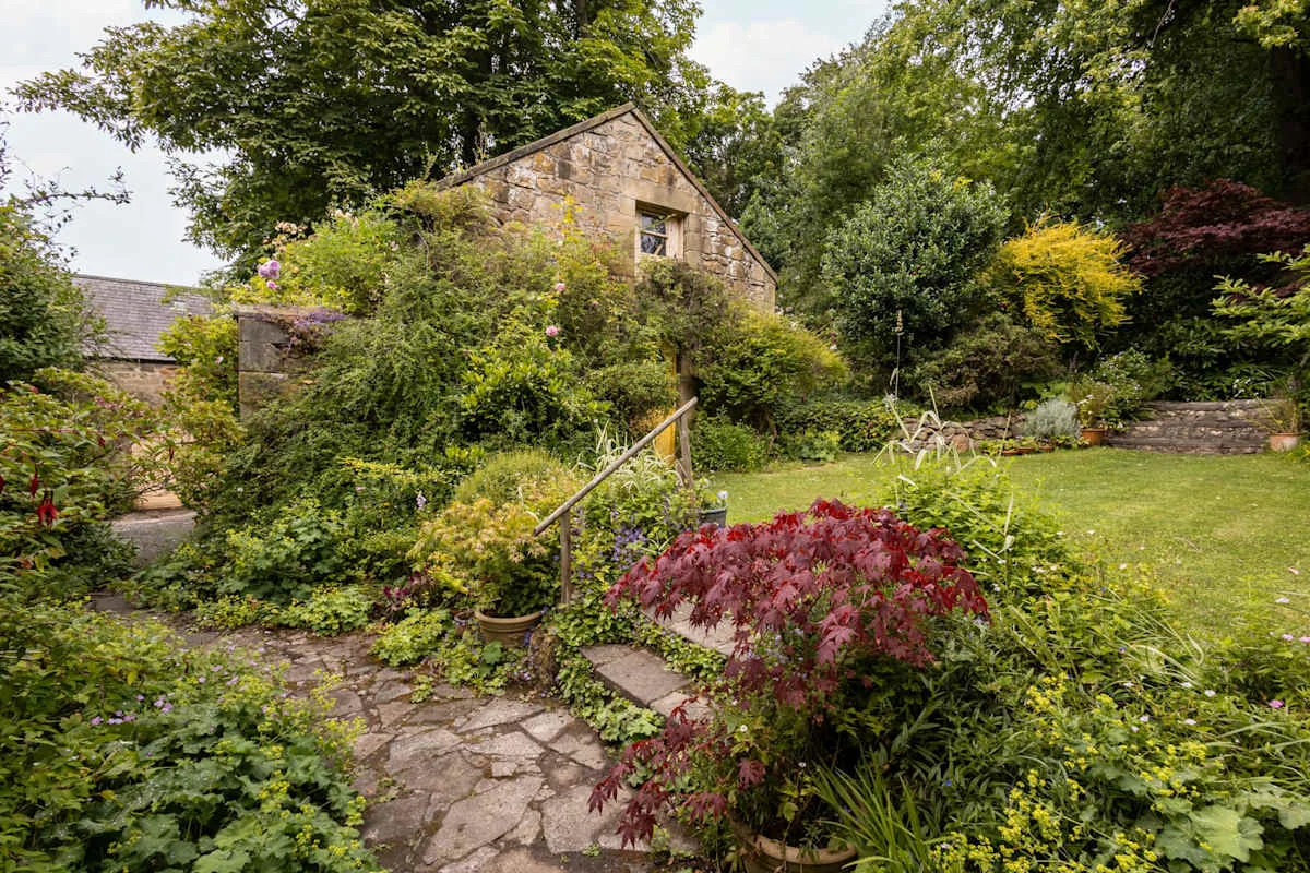 A stone garden path leads through lush landscaping toward a cottage.