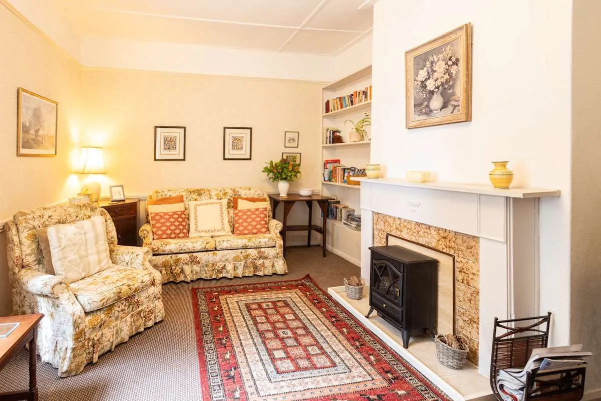 A living room with patterned seating, a fireplace, and a red rug.