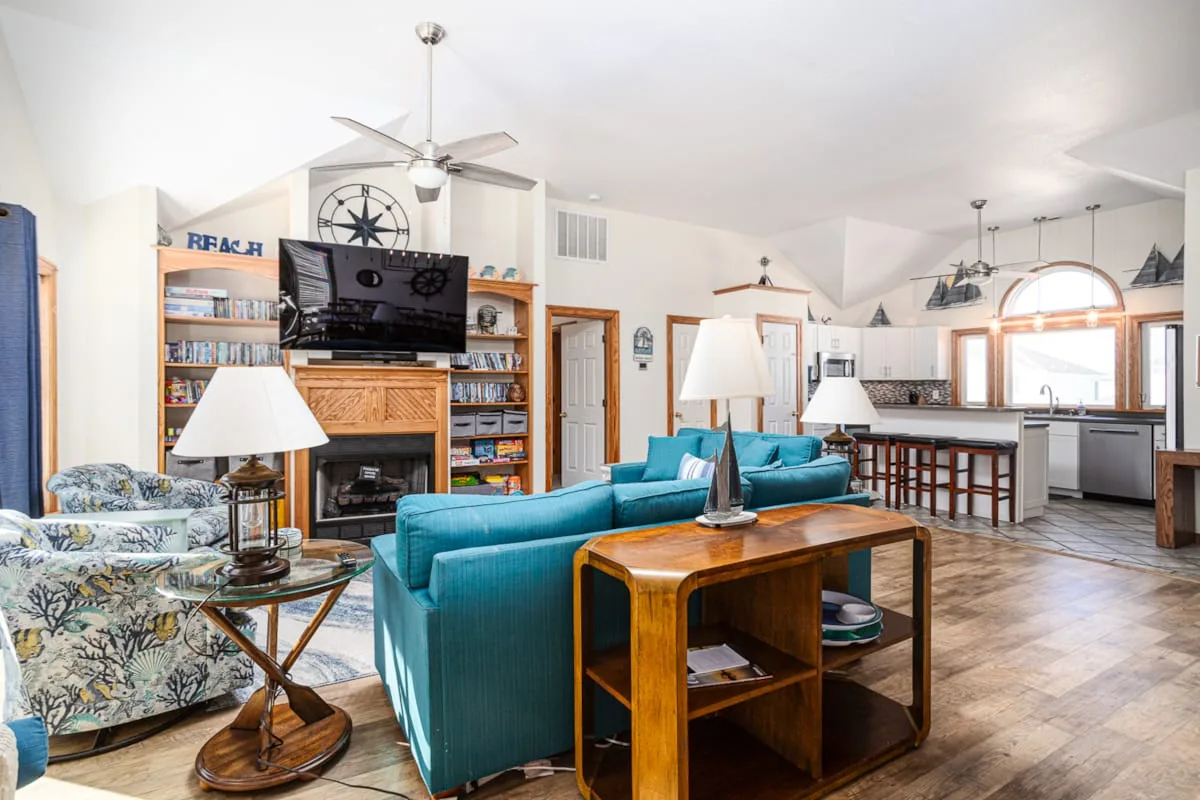 Una sala de estar y cocina de planta abierta con asientos color turquesa y una mesa de centro de madera.