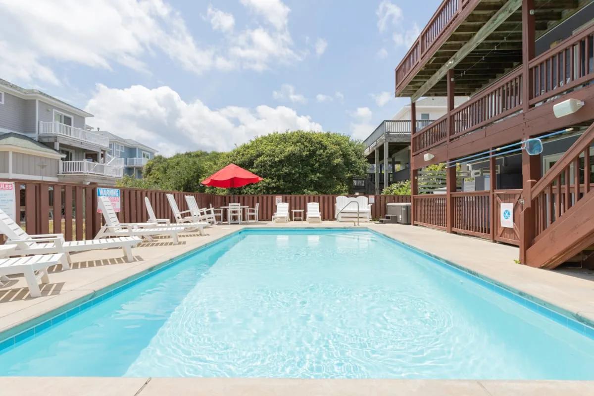Una piscina al aire libre está rodeada de asientos reclinables y una terraza de madera.