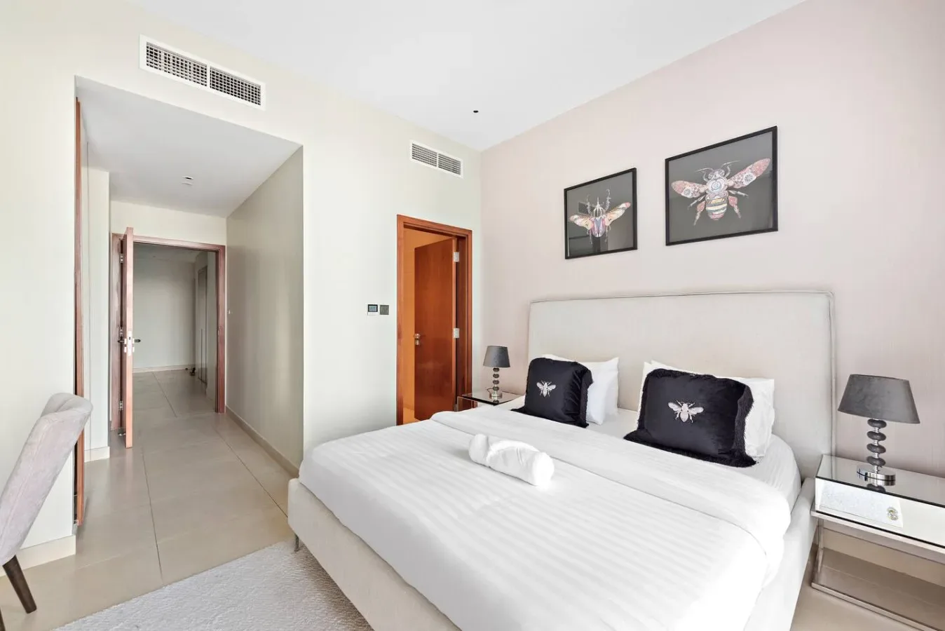 Un dormitorio luminoso con una cama bien hecha y cuadros enmarcados sobre el cabecero.