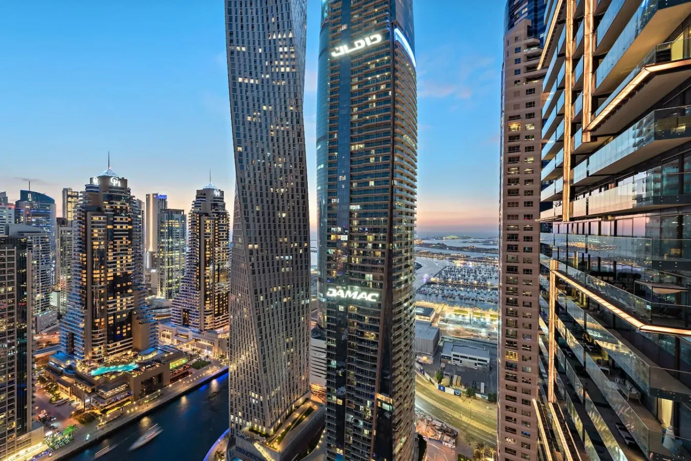 Panorámica urbana al atardecer, con edificios altos iluminados junto a un canal.