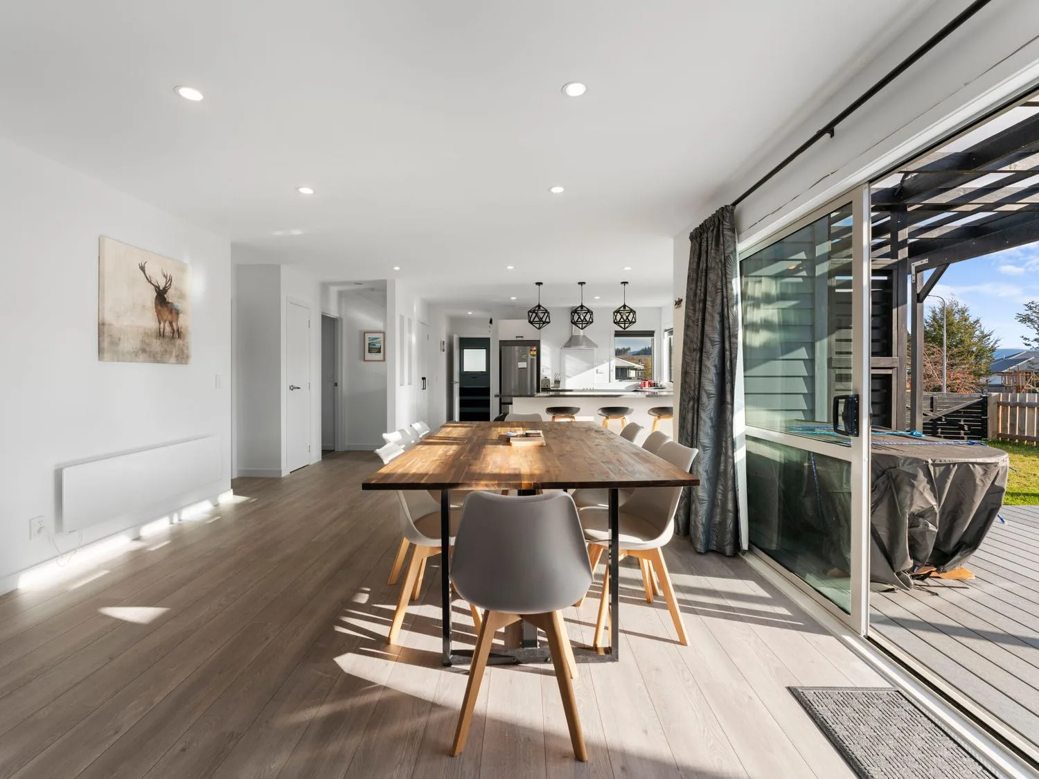A dining area with a wooden table and white chairs next to a sliding glass door leading to an outdoor deck with a covered grill at Motuoapa Getaway - Lake Taupo Holiday Home in Motuoapa