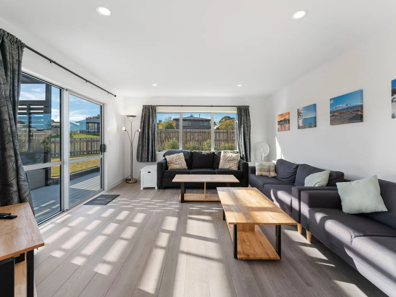 Una sala de estar con dos sofás, mesas de centro de madera, una lámpara de pie y fotos en la pared en Motuoapa Getaway - Lake Taupo Holiday Home, en Motuoapa