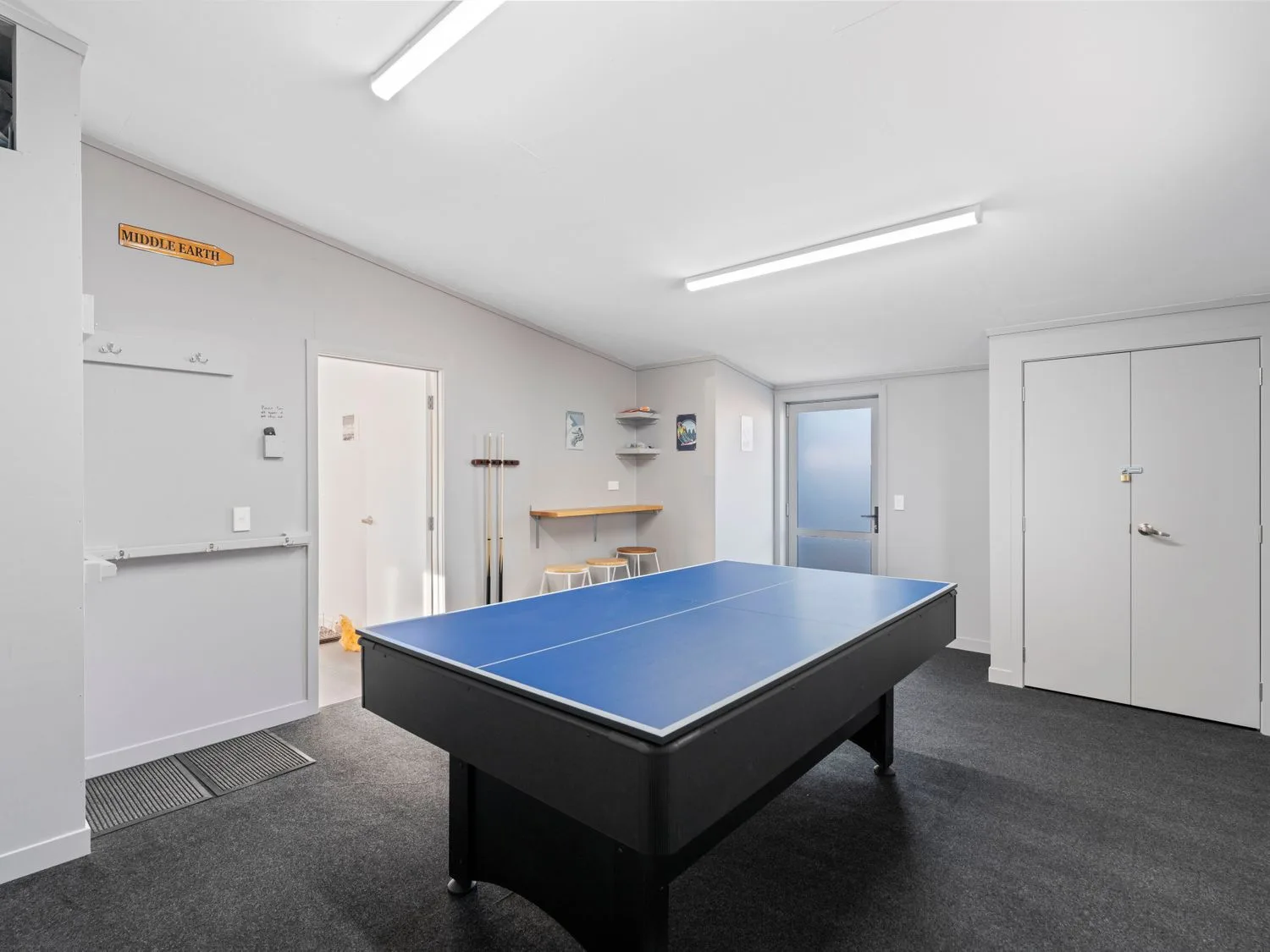 A game room with a blue ping-pong table and pool cues mounted on the wall.