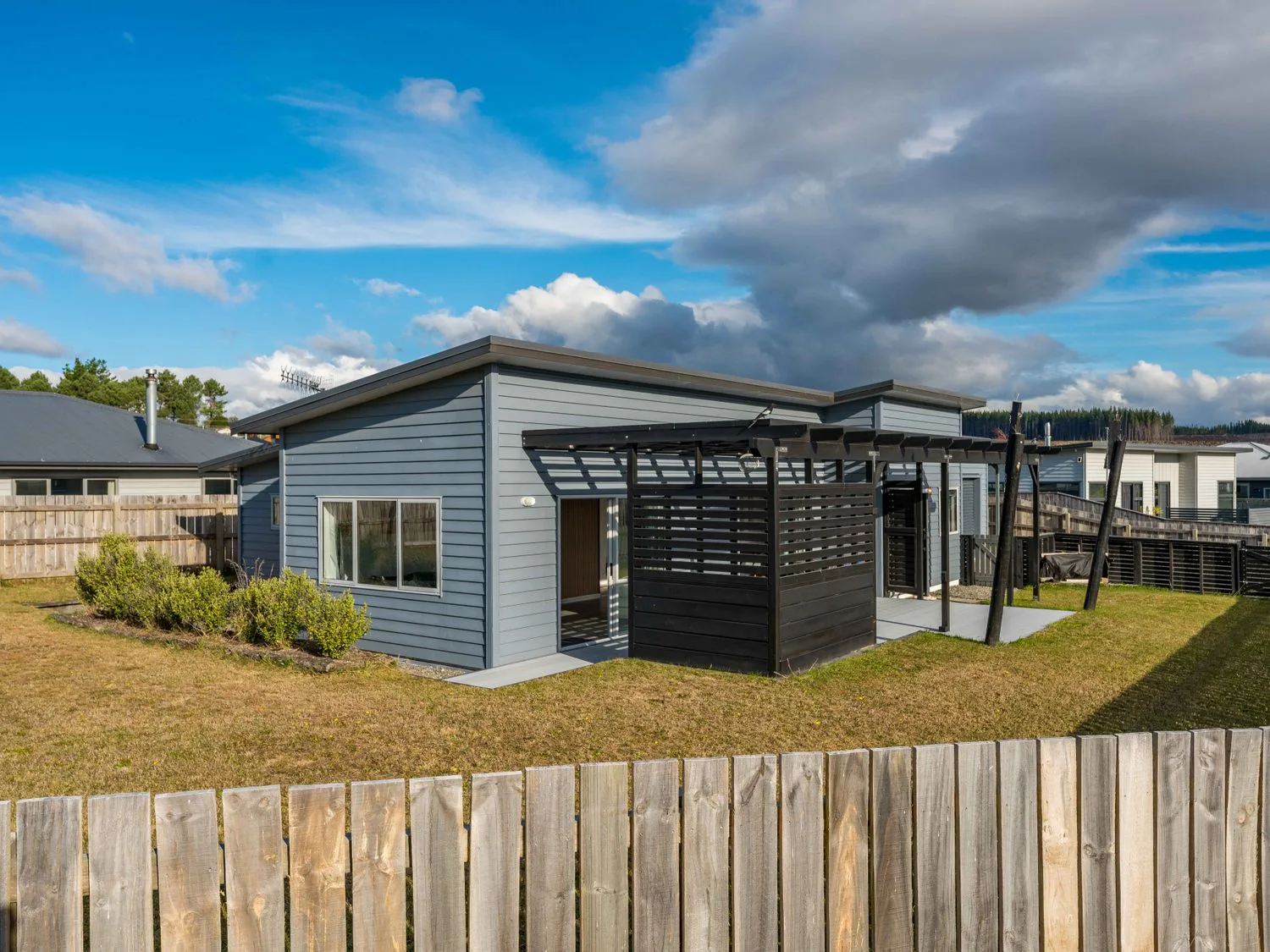 A single-story house with blue siding and a fenced yard with grass and shrubs at Motuoapa Getaway - Lake Taupo Holiday Home in Motuoapa
