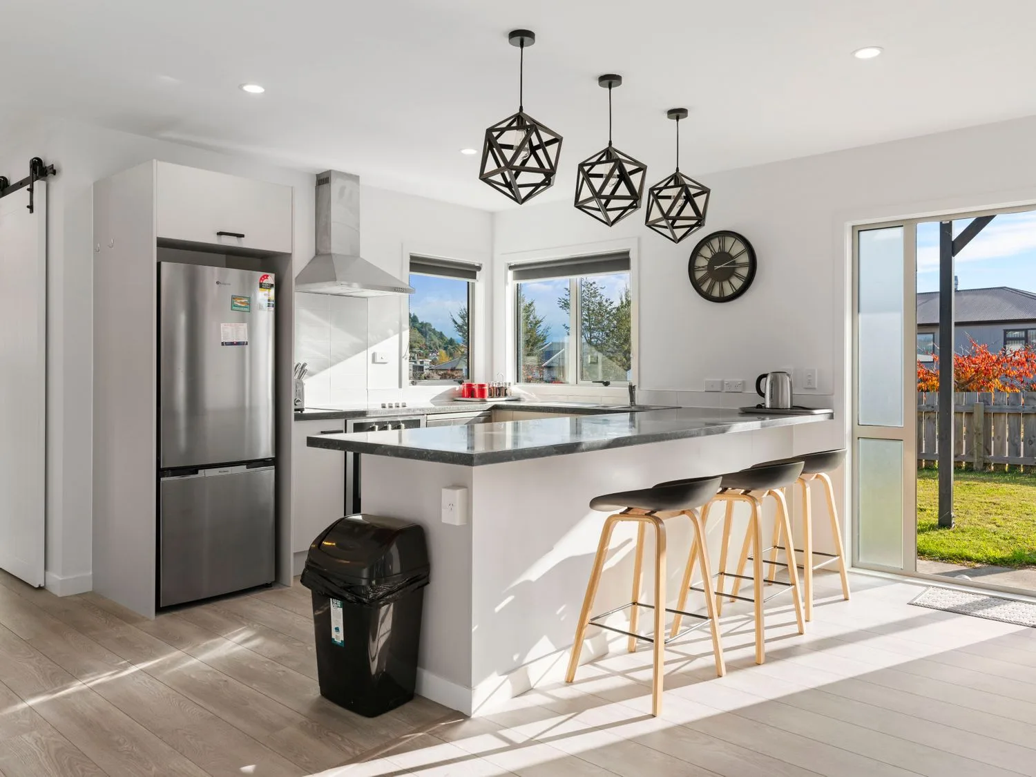 A kitchen with a refrigerator stove island counter with three stools and a clock on the wall at Motuoapa Getaway - Lake Taupo Holiday Home in Motuoapa