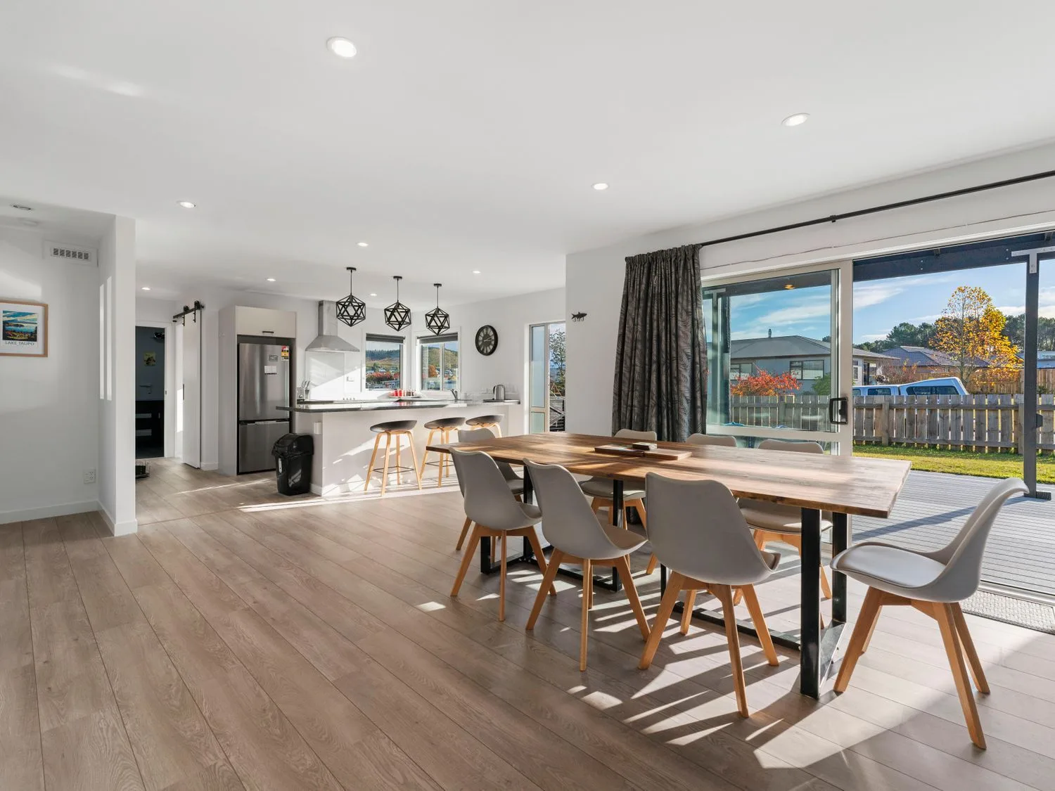 A dining area with a wooden table and chairs next to a kitchen with bar stools and pendant lights at Motuoapa Getaway - Lake Taupo Holiday Home in Motuoapa