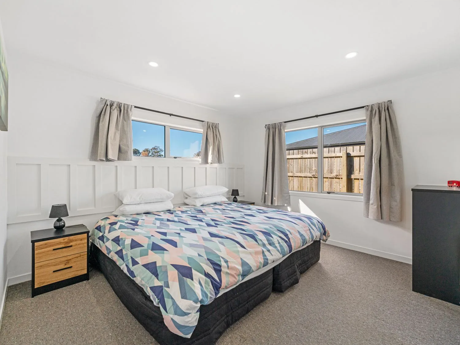 A bedroom with a large bed two bedside tables and two windows with curtains at Motuoapa Getaway - Lake Taupo Holiday Home in Motuoapa