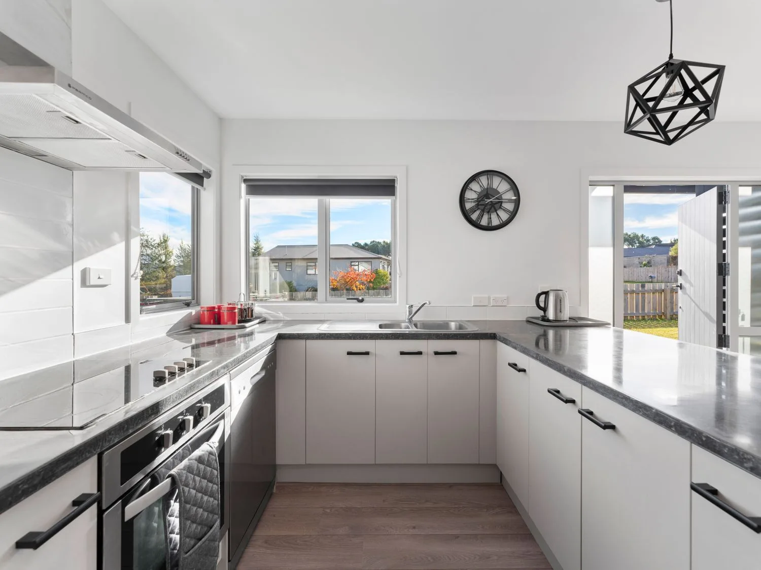 A bright kitchen with white cabinets and dark countertops, with windows and an open doorway.