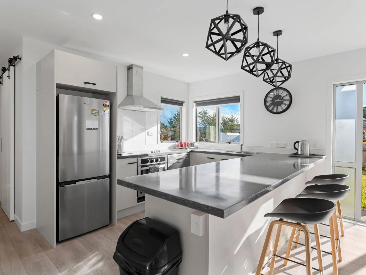 A kitchen with a refrigerator oven bar stools and pendant lights at Motuoapa Getaway - Lake Taupo Holiday Home in Motuoapa