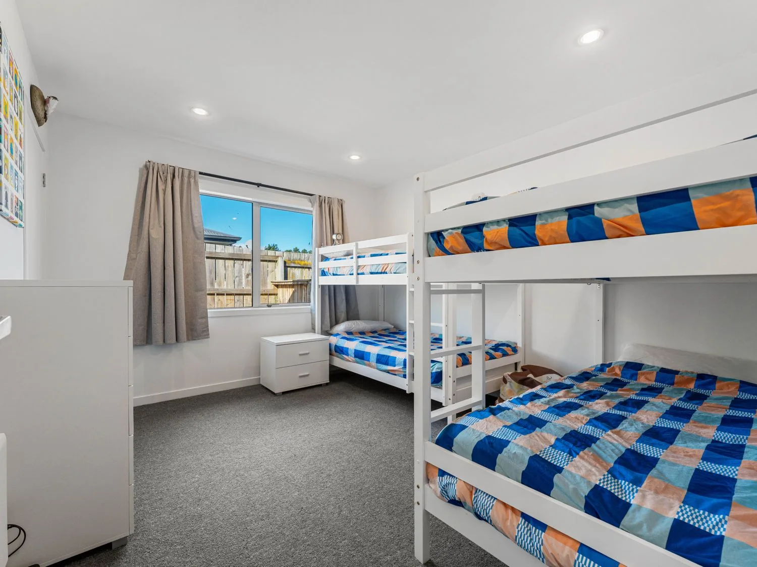 A bedroom with white bunk beds, colorful bedding, a dresser, and a curtained window.