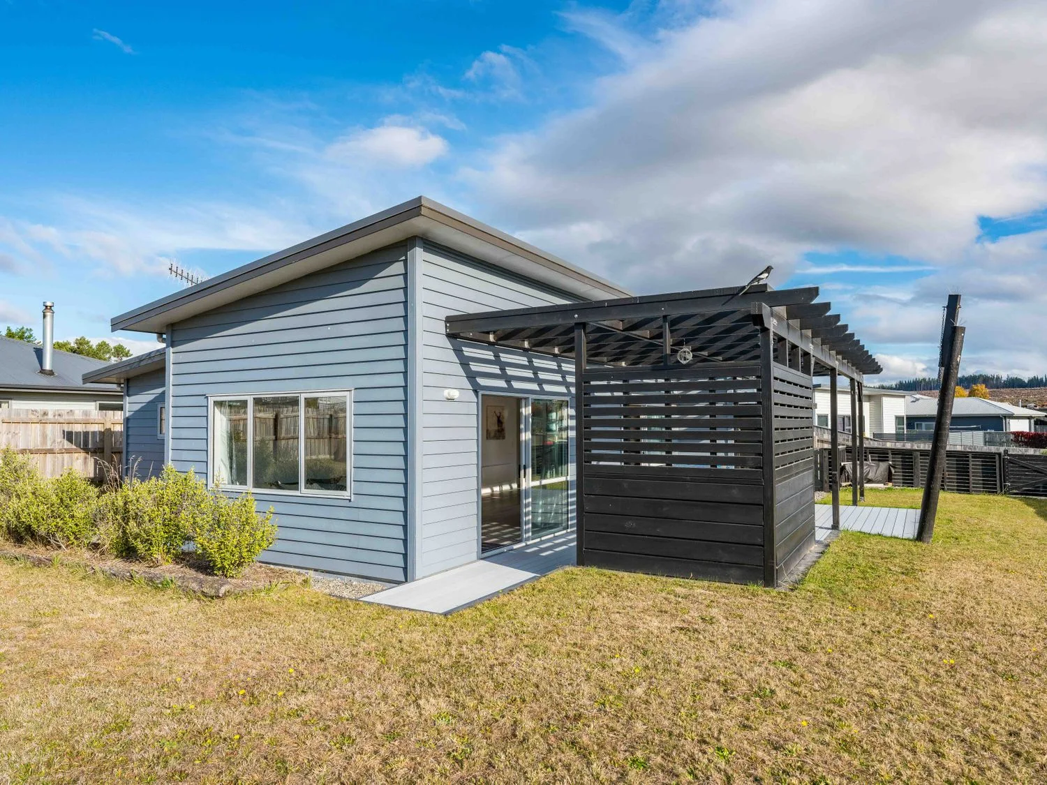 A single-story house with blue siding and a black pergola on the side at Motuoapa Getaway - Lake Taupo Holiday Home in Motuoapa