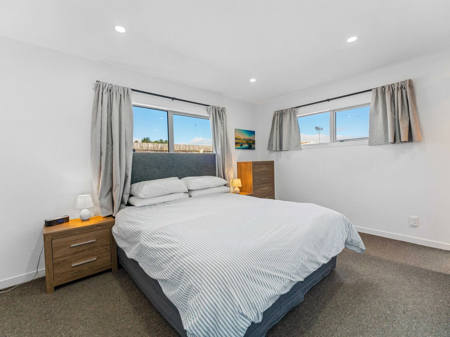 A bedroom with a bed a bedside table with lamp and alarm clock and a chest of drawers with lamp at Motuoapa Getaway - Lake Taupo Holiday Home in Motuoapa